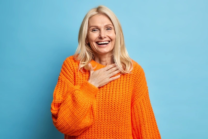 A woman with her hand to her chest, smiling at her restored teeth