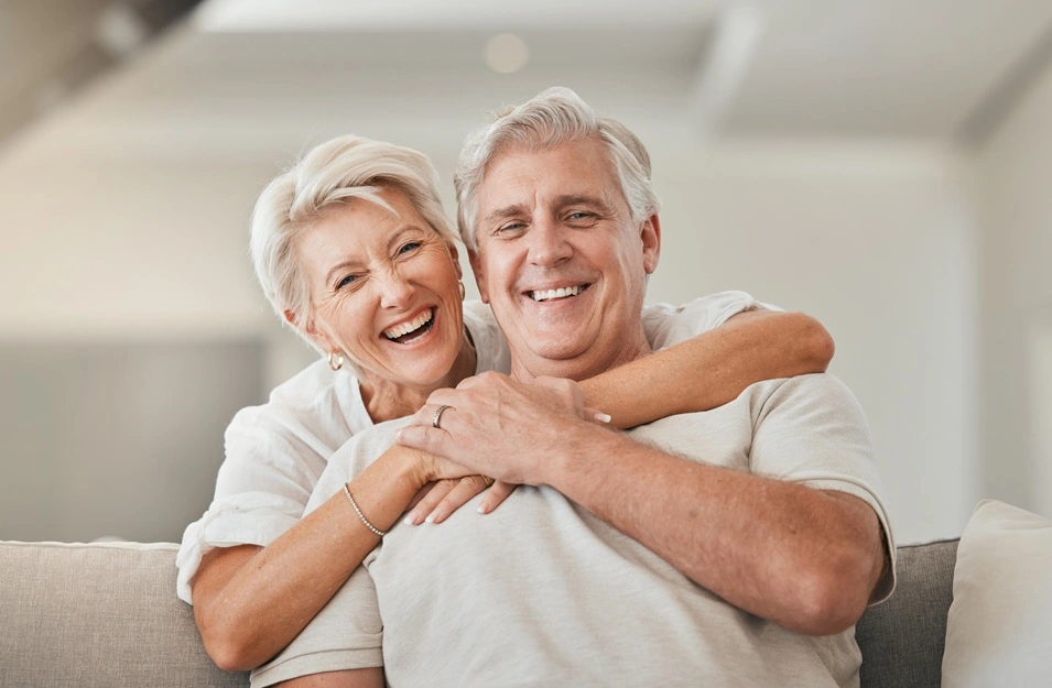 An older couple smiling together at home after denture treatment